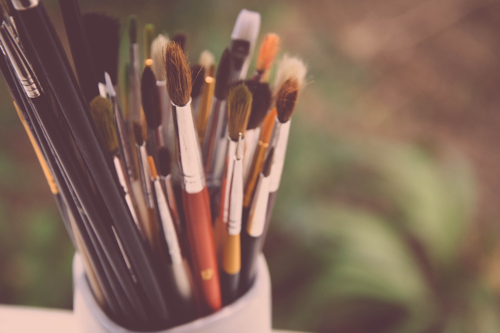 A white vase full of paintbrushes.