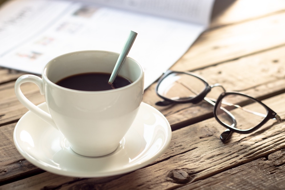 Cup of coffee and reading glasses on wooden table.